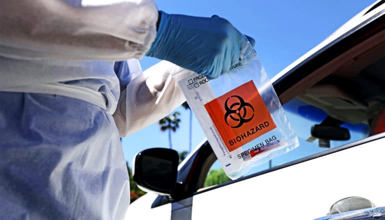 A health worker holds a biohazard bag with a COVID test sample