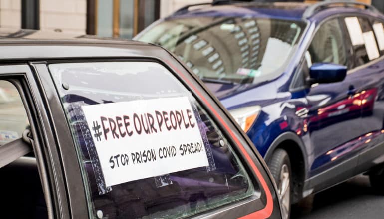 sign on car window says "#FreeOurPeople stop prison covid deaths"