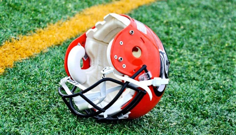 An orange football helmets sits on its side on a green field