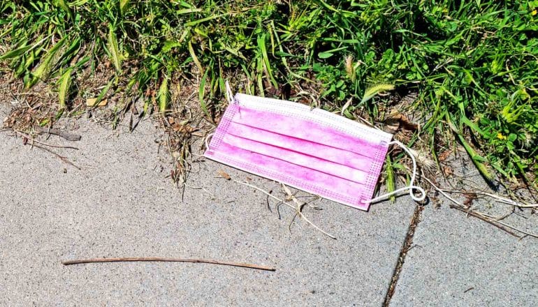 A pink mask sits on the sidewalk next to some grass