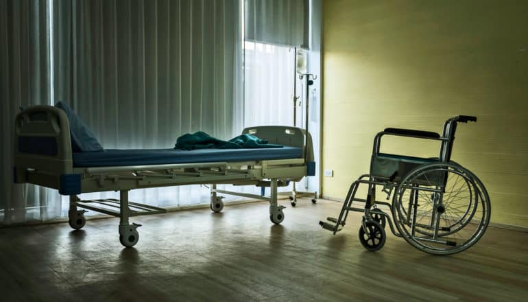 empty hospital bed and wheelchair in dim room