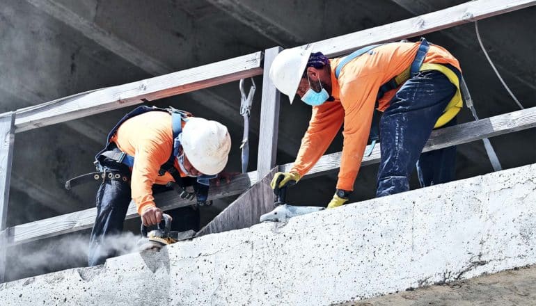 Two construction workers lean down to work on a concrete floor