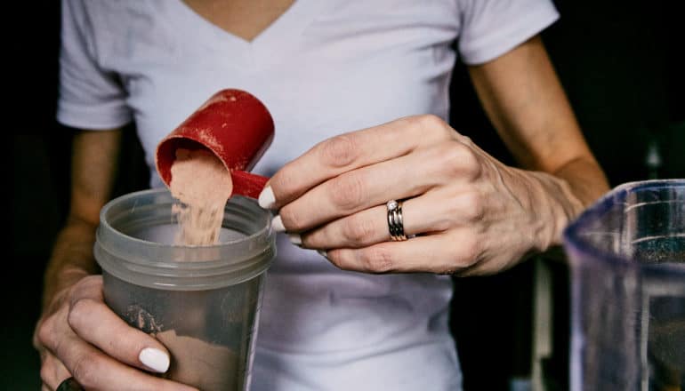 hand tips protein powder into blender