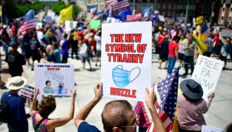 protestor holds sign with mask on it: "The new struggle of tyranny / muzzle"