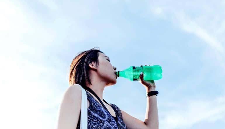 A young woman drinks soda from a green bottle