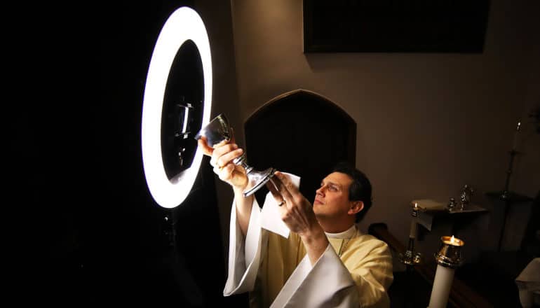 reverend holds chalice of wine up to phone in ring light