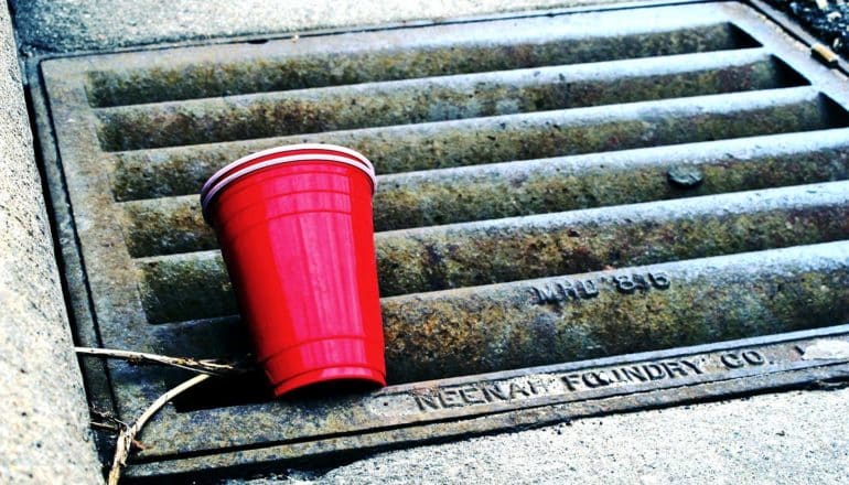 A red solo cup sits on a sewer drain on the street