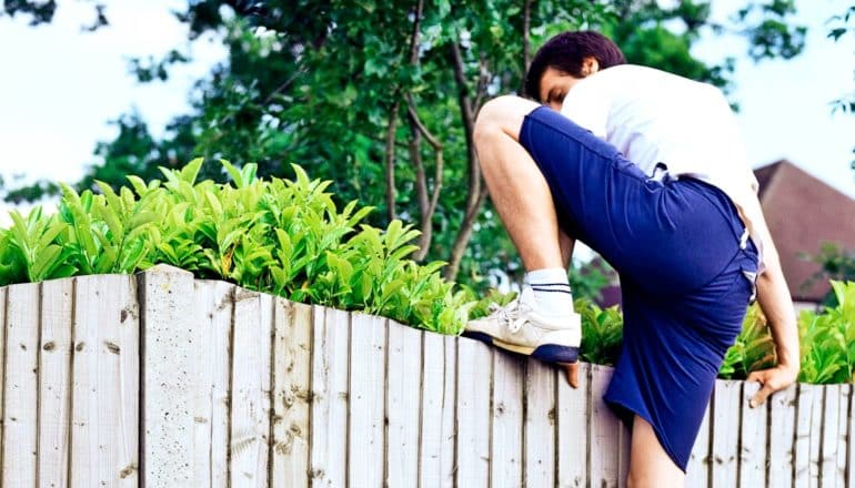 A teenager climbs over a wooden fence