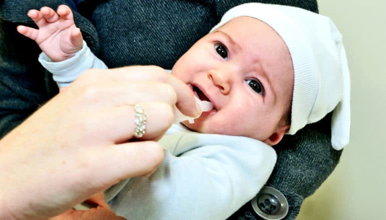 A baby takes medicine orally from a parent