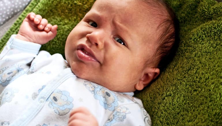 A baby looks at the camera while laying on a green blanket