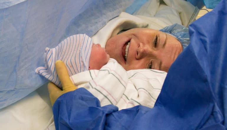 newborn baby held for mother to see during c-section