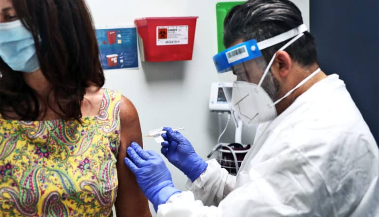 A woman is about to get a trial COVID-19 vaccine from a researcher in full PPE