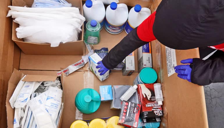 gloved hand reaches into box of assorted PPE