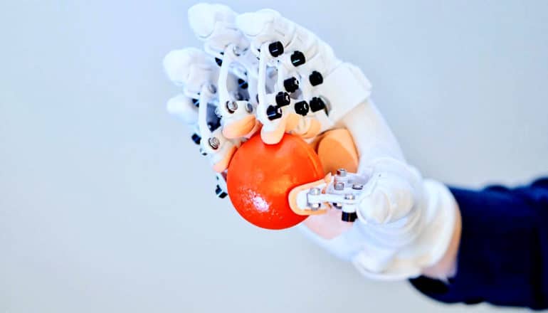 A person wearing the HandMorph glove grips a small orange ball