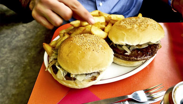 A person grabs a french fry off a plate with two burgers on it