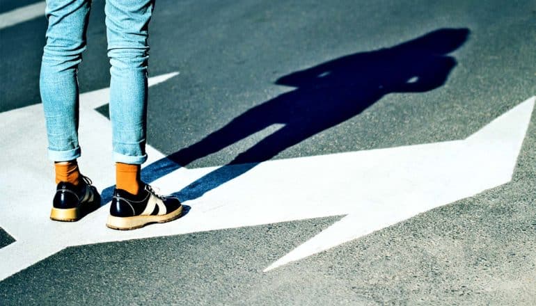 A person stands on asphalt between arrows pointing in different directions