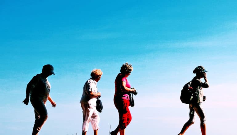 Four older women walk against a blue sky in the background