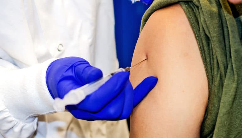 A patient gets an injection in the arm from a health worker wearing blue gloves