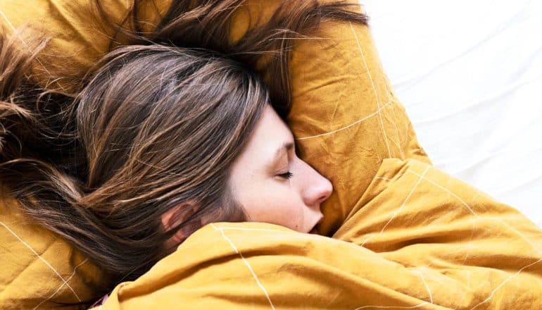 A woman sleeps on yellow sheets and blankets