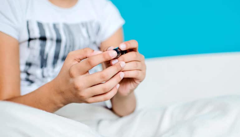 A girl checks her blood sugar while sitting up in bed