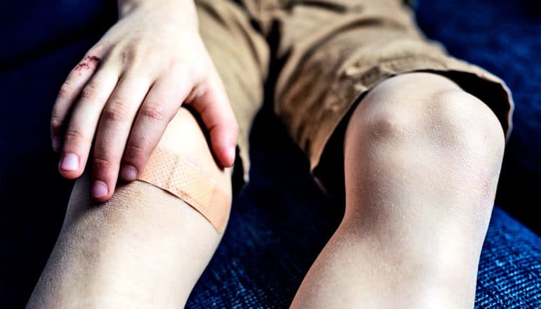 A boy holds his knee, which has a small bandage on it