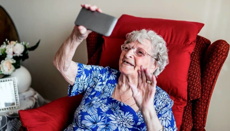 elderly person in recliner holding up phone and waving