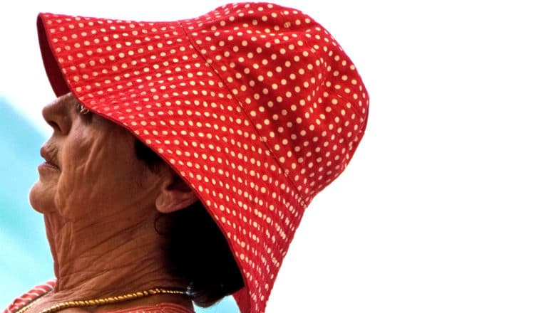 An older woman wearing a red hat leans back against a white background