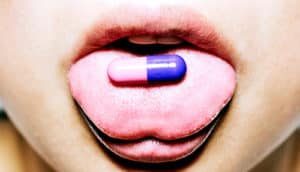 A young woman has a pink and purple pill on her tongue