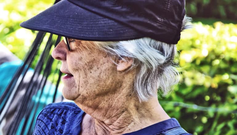 A woman in blue wearing a cap looks out from a garden seat