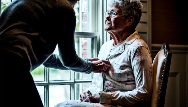 A caregiver helps an older woman with her pajama buttons