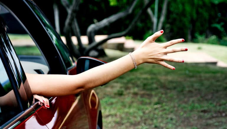 A woman sticks her arm out of an open car window