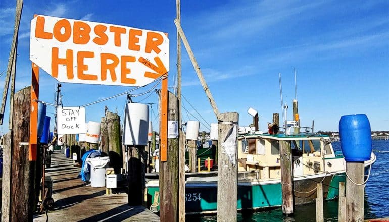 A fishing boat at a dock with a sign that reads "Lobster here"