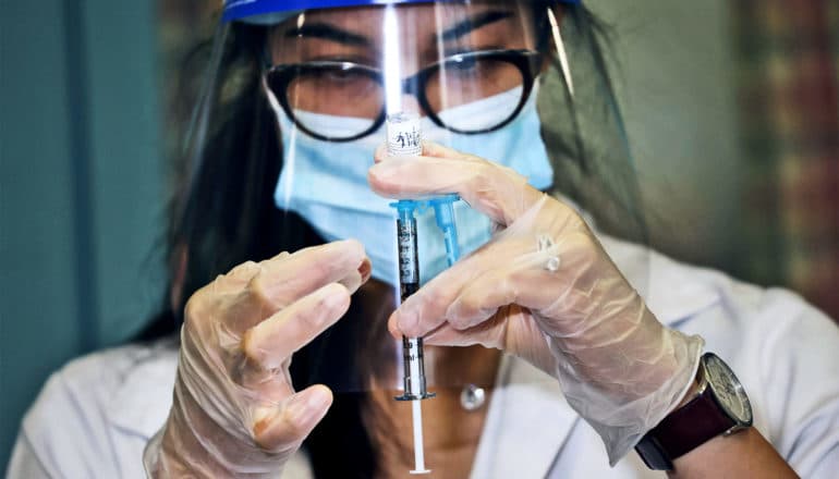 A pharmacist fills a syringe with the COVID-19 vaccine