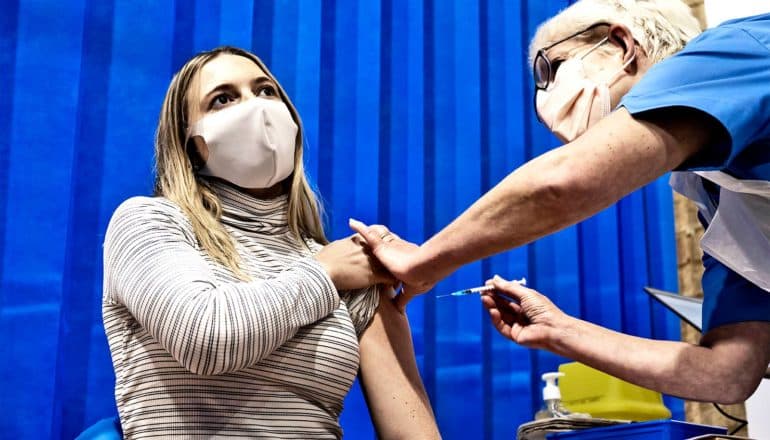 A young woman rolls up her sleeve to get a COVID-19 vaccine