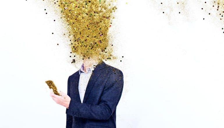 A man reads his phone as golden glitter bursts over his face and head