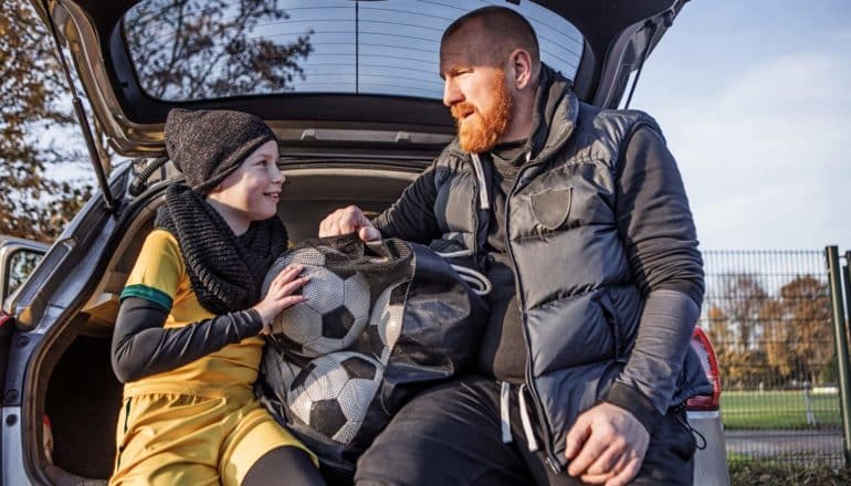 father and daughter sit in back of car with soccer balls