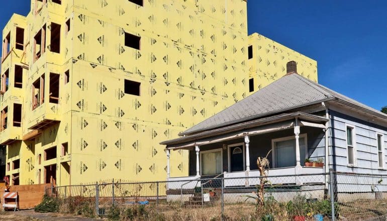 apartment building under construction next to small, slightly unkempt home