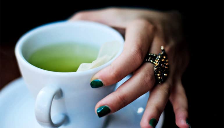 A woman with green nail polish picks up a cup of green tea