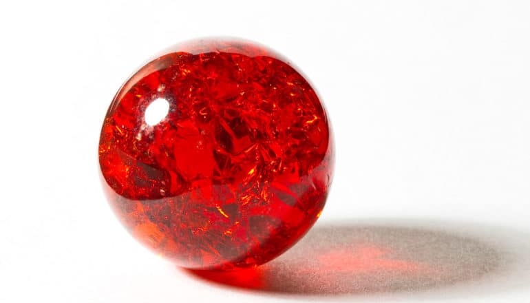 A red marble sits on a white background with light shining through it