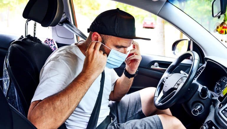 A man sitting in a car puts a mask on