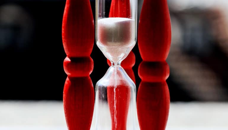 Sand falls through an hourglass with red wooden struts