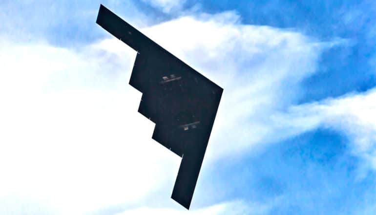 A stealth bomber plane flies through blue skies