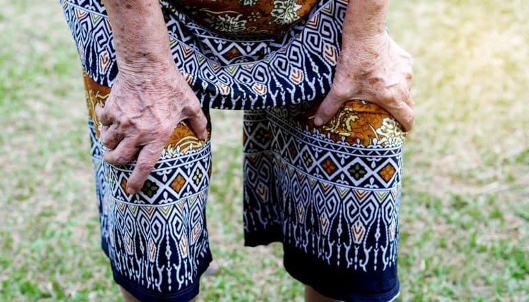 A woman bends down to grab her knees in pain