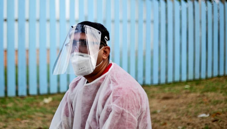 weary-looking person in PPE sits outdoors