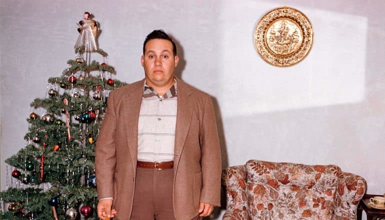 retro shot of befuddled person standing in front of xmas tree, chair