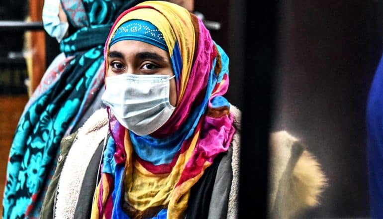 A woman wearing a headscarf and face mask waits for food