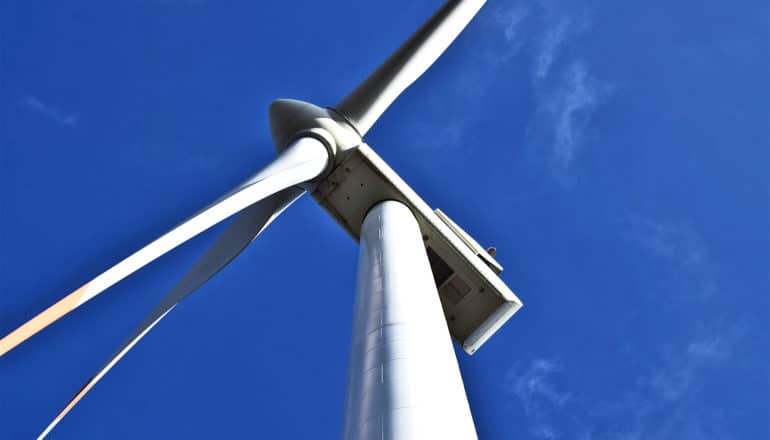 A wind turbine seen from below against a blue sky