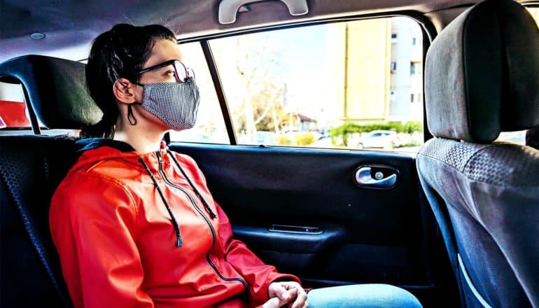 A young woman in a face mask sits in the back seat of a car