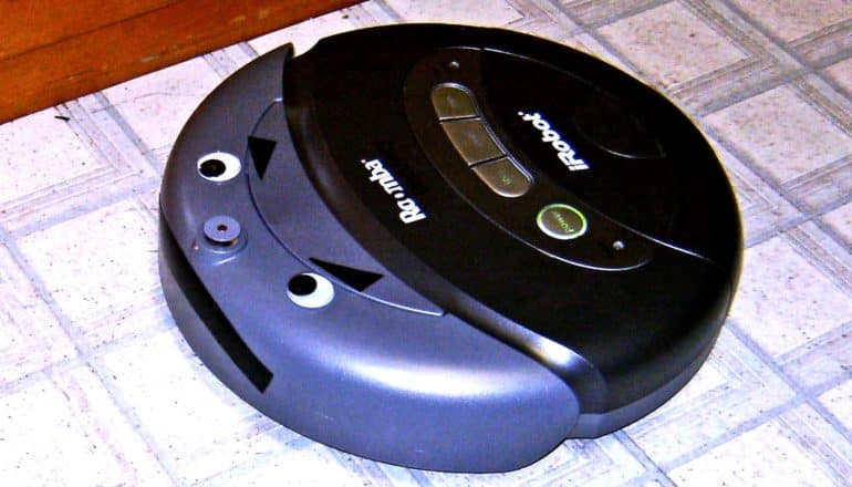 A robot vacuum cleaner has googly eyes on it and angry eyebrows and a mouth made of tape