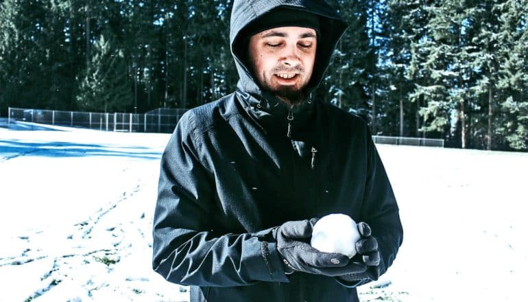 A man holds a snowball and looks down at it with a smile